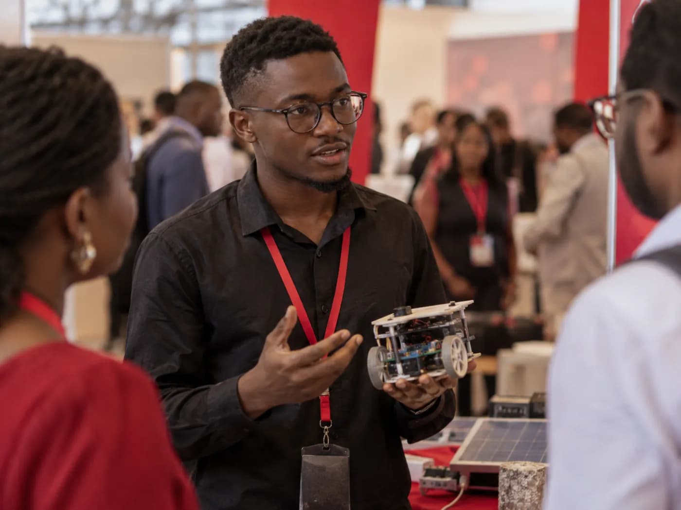 Jeune innovateur présentant un prototype sur un stand, foule floue en arrière-plan